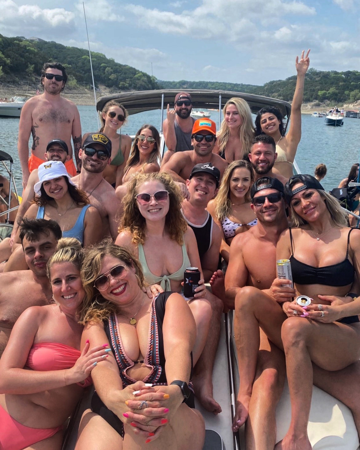 Excited bachelorette party group in matching blue swimsuits posing on a pontoon boat with drinks.