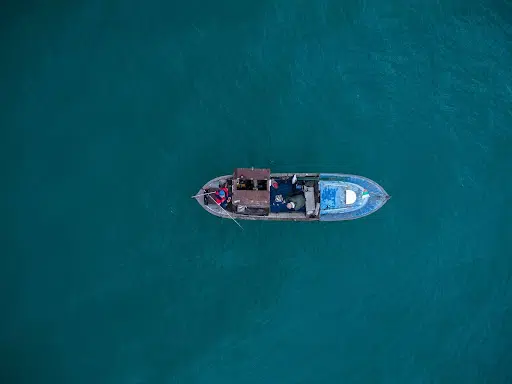 Aerial view of small fishing boat floating alone on deep blue water.