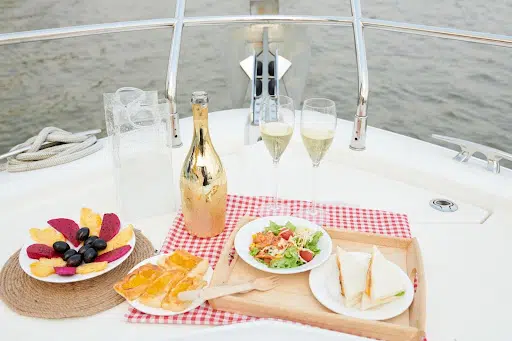 Luxury boat table set with champagne, glasses, fresh salad, fruit, and sandwiches.