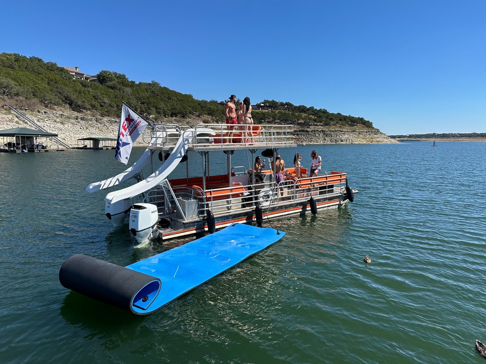 Orange and white double-decker pontoon party boat with slide and people relaxing on deck.