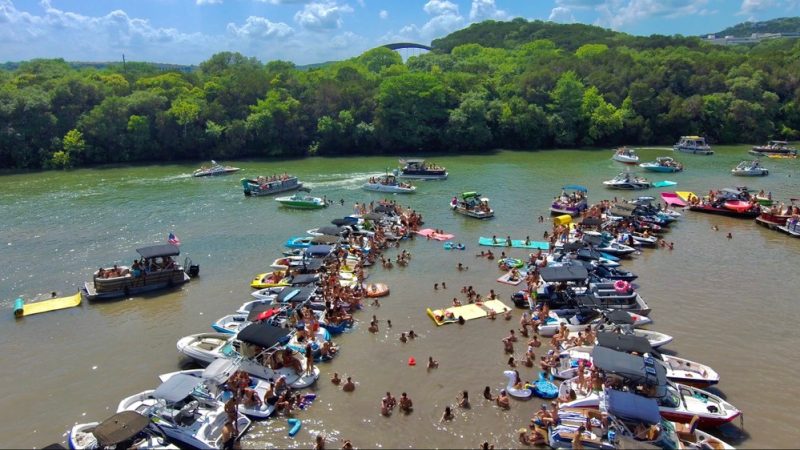 Lake boat party cove aerial view – Aerial shot of dozens of boats tied together with large crowds of people swimming and partying in a cove.